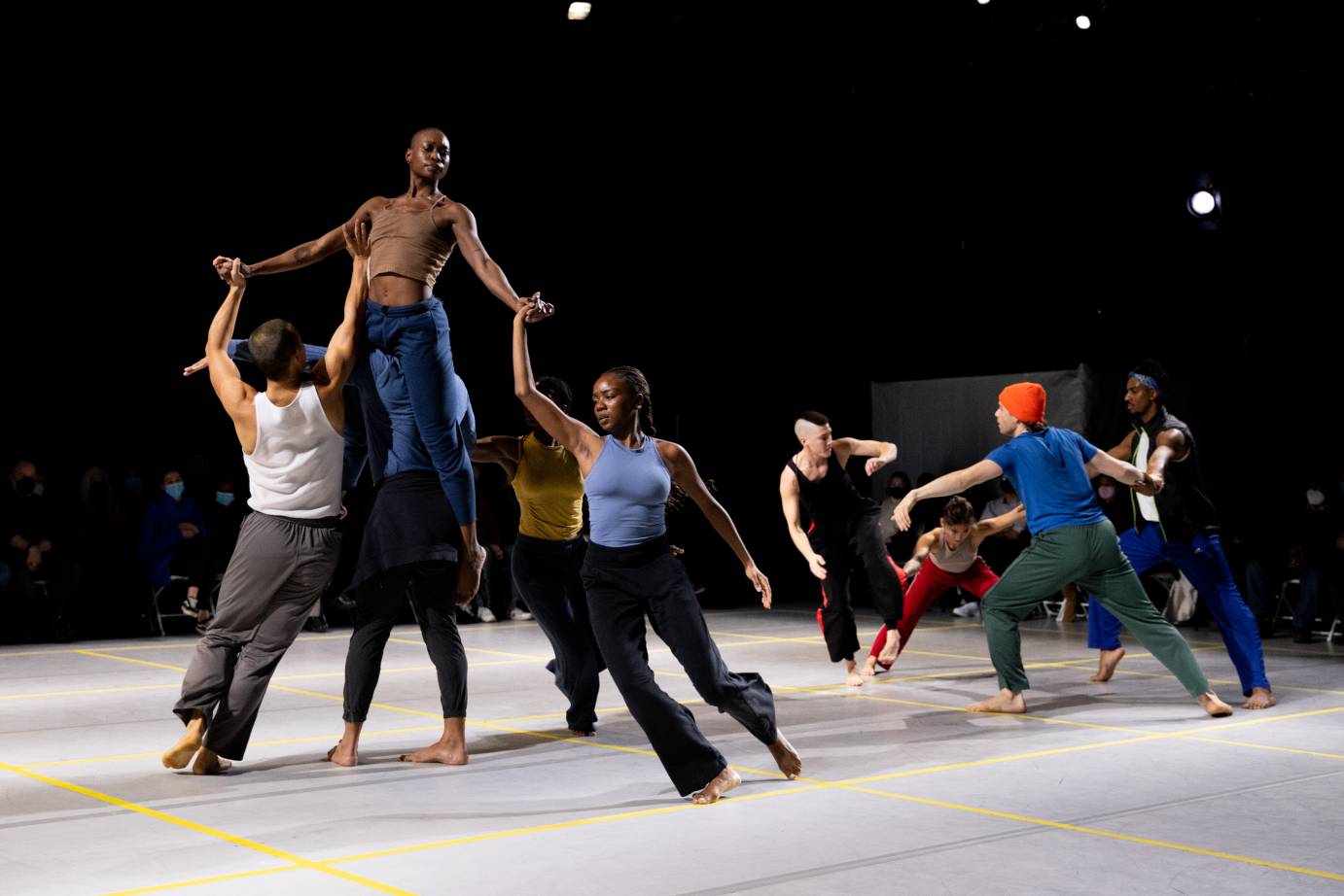 two circles of dancers of multiple skin tones and wearing workout clothes appear to be involved in the motions of turning and lifting